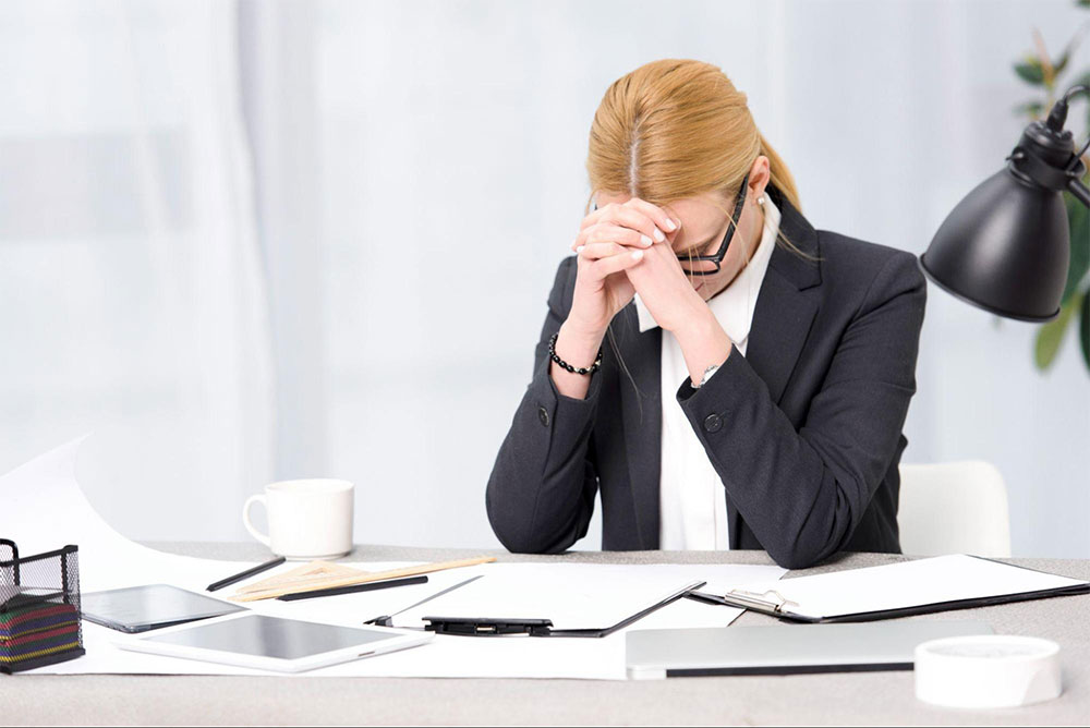 Woman in a suit with eyes closed and hands clasped against her forehead